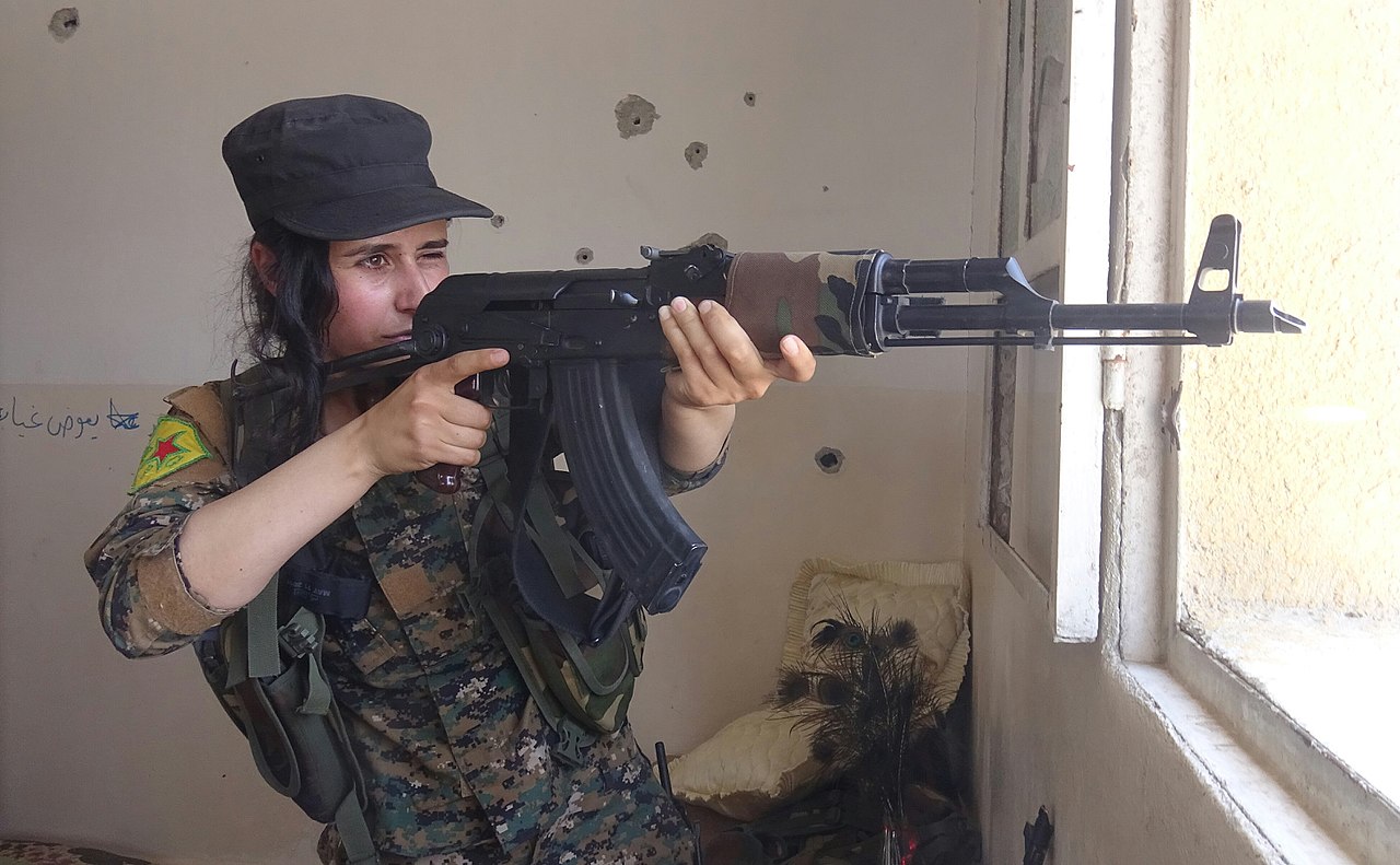 A soldier with the YPJ aims her rifle out the window 2.jpg