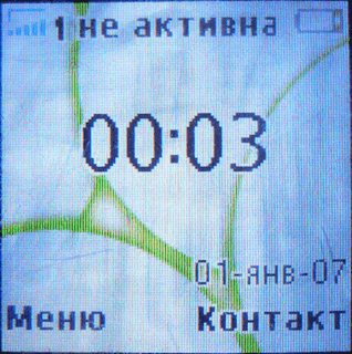 Главный экран телефона Sony Ericsson K220i отображает индикаторы уровня сети и заряда акумулятора, дату, часы и программные подписи верхних кнопок.