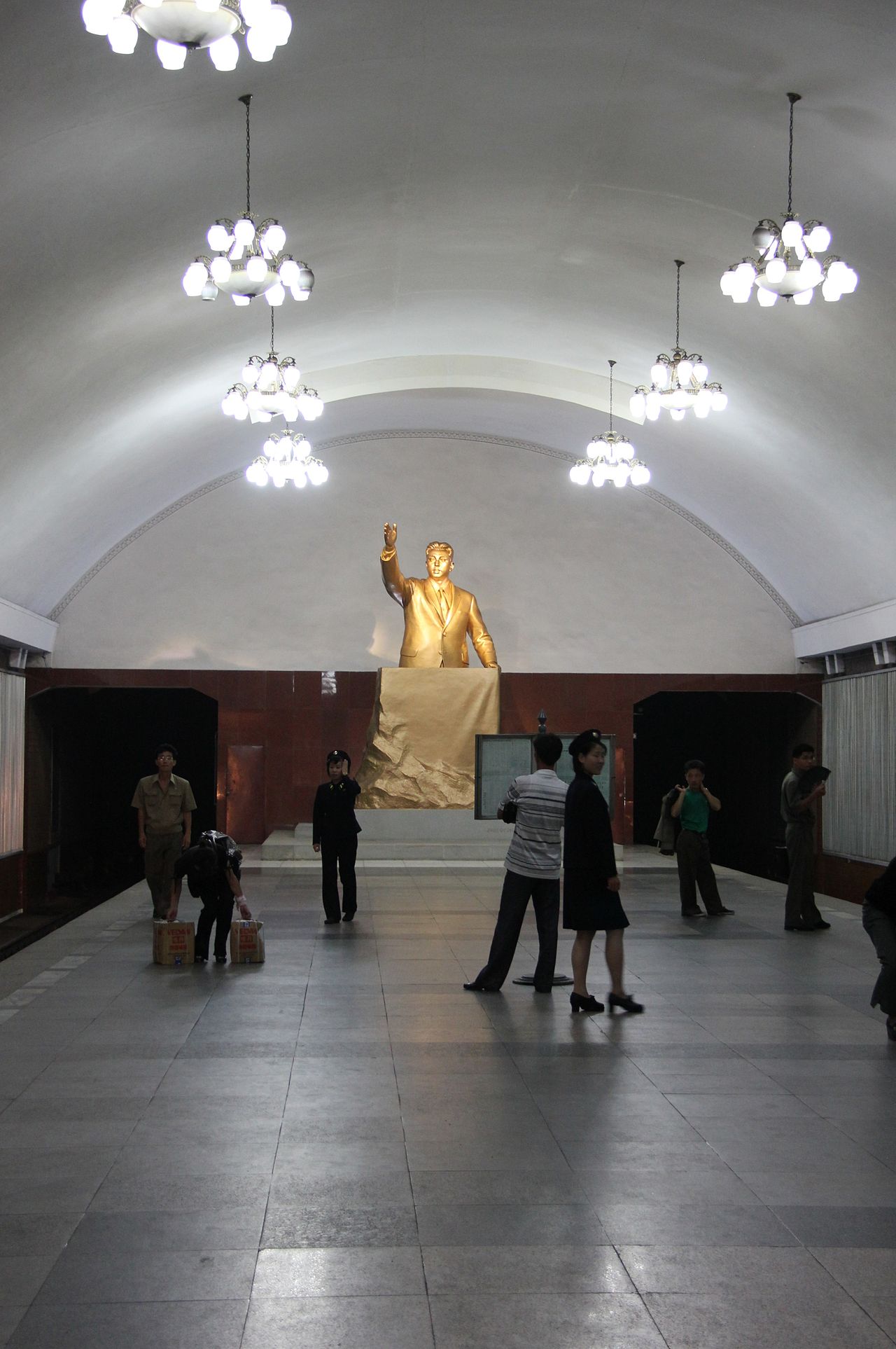 Платформа станции, статуя Ким Ир Сена и стенды с газетой "Нодон синмун"